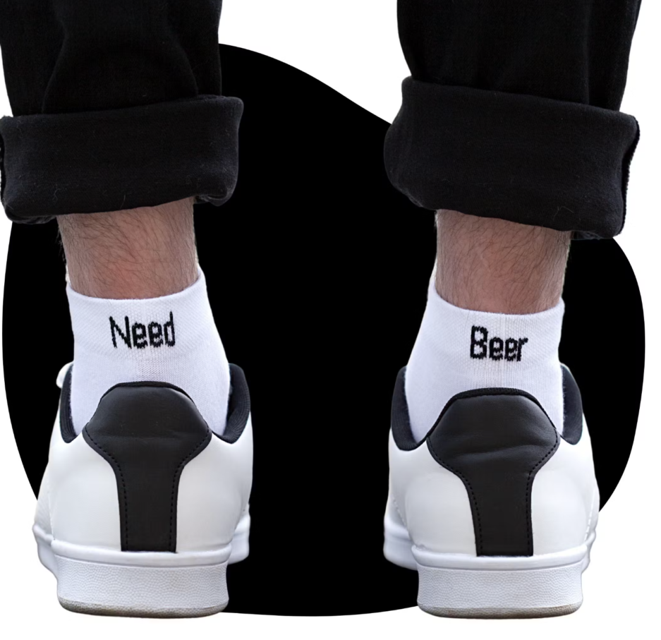 (Chaussettes Need Beer) Chaussettes blanches avec écrit en noir "Need" sur la chaussette gauche et "Beer" sur la chaussette droite. Les deux ensemble font les Chaussettes Need Beer"